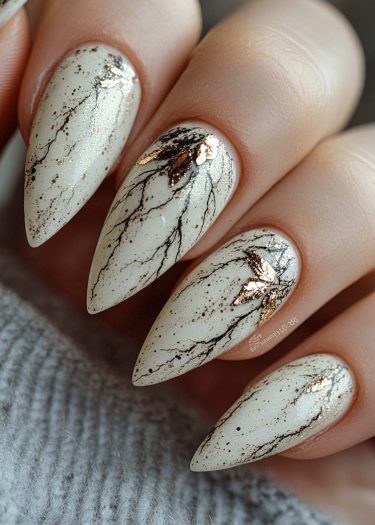 Stunning stiletto nails with gold leaf and marble design on a soft gray background.