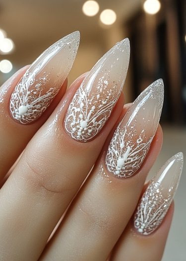 Elegant stiletto nails with ombre effect, intricate white patterns, and sparkling accents.