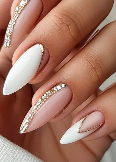 Elegant almond-shaped white and nude nail art with gold accents and rhinestones for a chic look.