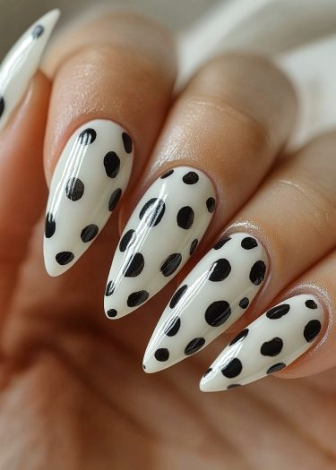 Elegant white stiletto nails with bold black polka dots for a modern nail design.