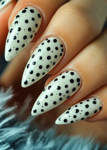 Elegant stiletto nails featuring glossy white polish and black polka dots on a textured blue background.