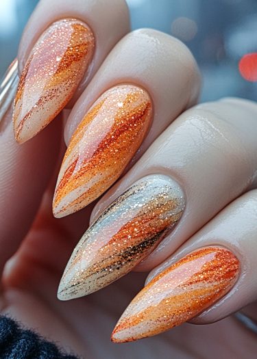 Stunning autumn gradient stiletto nails with glitter in warm hues of orange and gold.