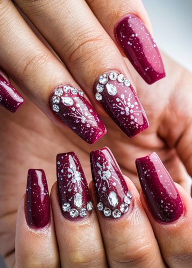 Elegant burgundy nail art with snowflake patterns and rhinestones for a festive look.