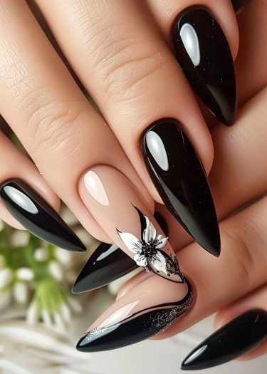 Elegant black stiletto nails with a detailed floral accent and sparkling embellishments.