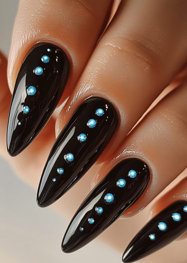 Stunning black stiletto nails adorned with blue rhinestones for a chic, elegant look.