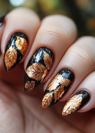 Elegant black almond nails adorned with gold leaf motifs for stunning nail art design.