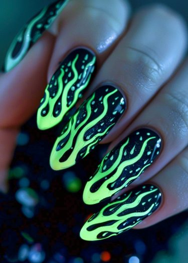 Bold black and neon green flame stiletto nail art design on long almond-shaped nails.