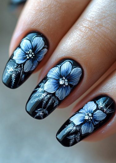 Elegant black floral nail art design with blue and white flowers and sparkling rhinestones.