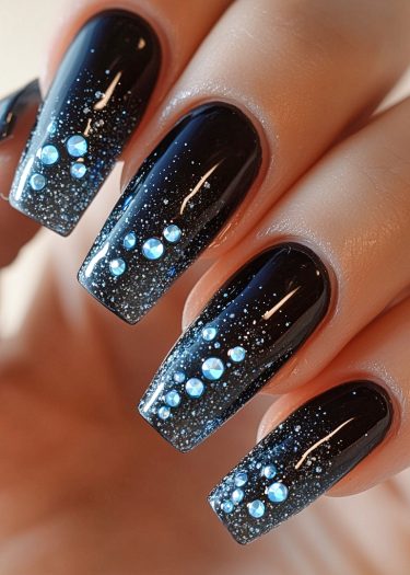 Elegant black glossy nails with glitter and blue rhinestones for a stunning nail art design.