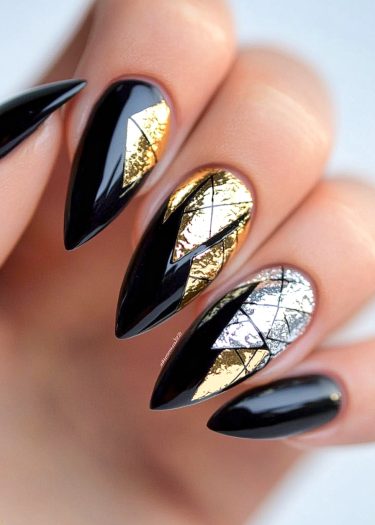 Stylish stiletto nails featuring glossy black polish and elegant metallic foil designs.