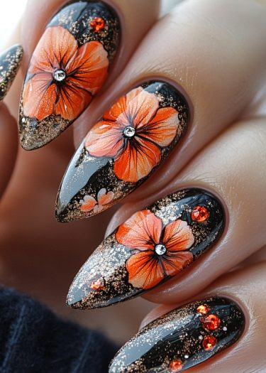 Elegant black and gold floral nail art featuring vibrant orange flowers and sparkling gemstones.