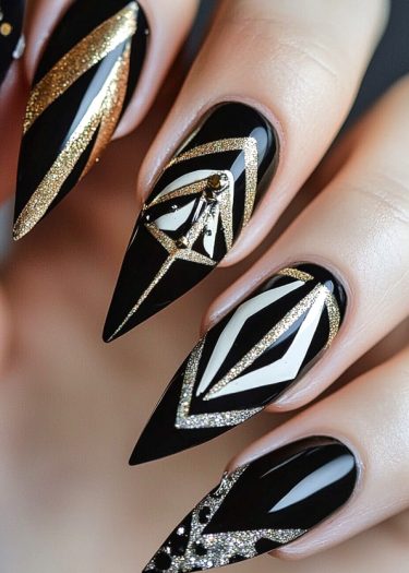 Elegant black and gold stiletto nails featuring intricate geometric art deco designs and rhinestones.