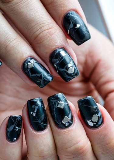 Elegant black marble nail art with silver foil accents for a chic, modern manicure.