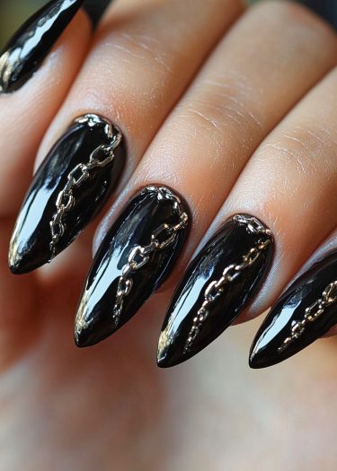 Glossy black stiletto nails adorned with silver metallic chains for a bold, elegant look.