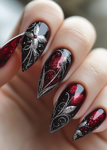 Elegant stiletto nails with black base, red glitter, and intricate silver designs for dramatic style.