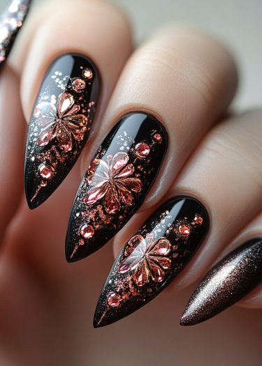 Elegant black stiletto nails with pink-rose gold floral designs and sparkling gemstones.