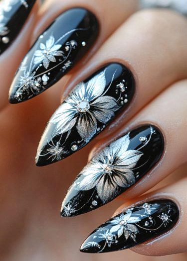 Elegant black and silver floral nail art design with rhinestones on almond-shaped nails.