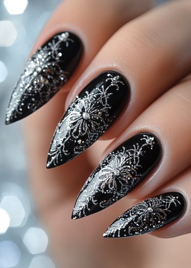 Elegant black stiletto nails adorned with intricate silver floral designs and sparkling rhinestones.