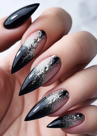 Glamorous black and silver gradient manicure featuring rhinestones on pointed stiletto nails.