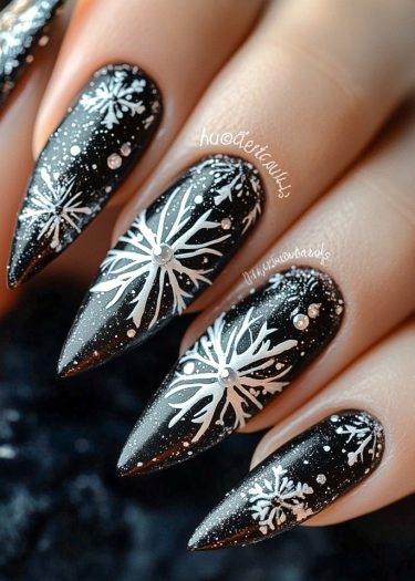 Elegant black stiletto nails with detailed white snowflakes and sparkling rhinestones for a winter look.