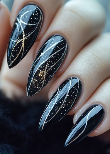 Elegant black stiletto nails with gold metallic swirls and glitter for stunning nail art.