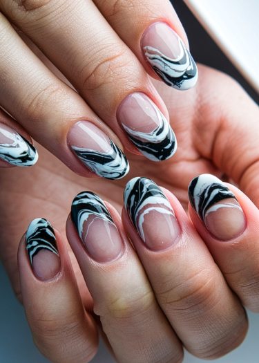 Stylish black and white marbled nail art on almond-shaped nails, showcasing intricate designs.