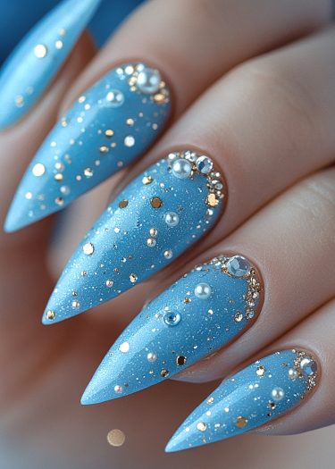 Elegant blue almond-shaped nails adorned with pearls, gold studs, and sparkling rhinestones.