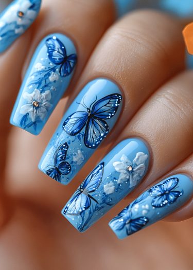 Pastel blue nail art featuring intricate blue butterflies and elegant white flowers with rhinestones.