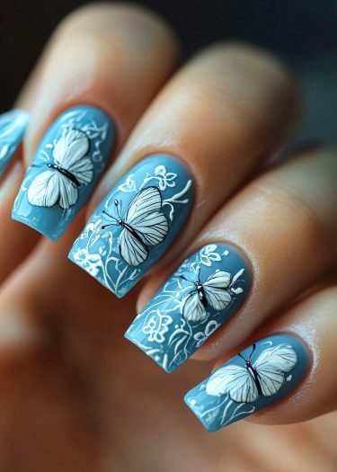 Elegant blue butterfly nail art with white floral designs for a nature-inspired look.