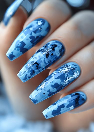 Stylish blue camouflage nail art with glitter on elongated coffin-shaped nails.