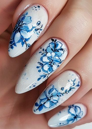 Elegant blue floral nail art on glossy white almond-shaped nails for a sophisticated look.