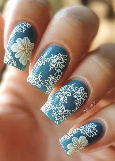 Elegant blue floral nail art with intricate white lace designs and three-dimensional flowers.