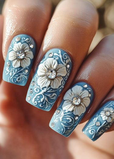 Elegant blue floral nail art with textured flowers and sparkling rhinestones for a sophisticated look.