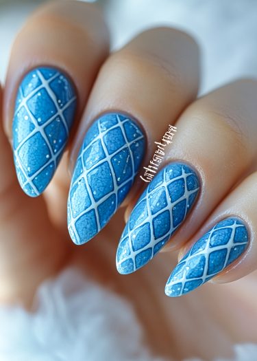 Stunning blue glitter nail art with white lattice design on elegant stiletto-shaped nails.