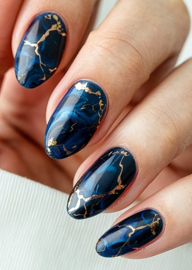 Exquisite blue and gold marble nail art on elegant oval-shaped nails.