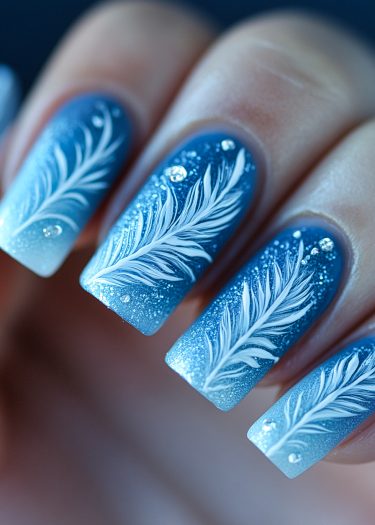 Elegant blue ombre nails with intricate white feather art and sparkling rhinestones.