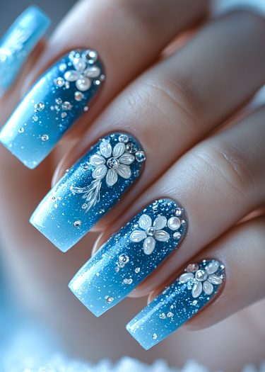 Elegant blue gradient nail art with floral designs and sparkling rhinestones for a luxurious look.