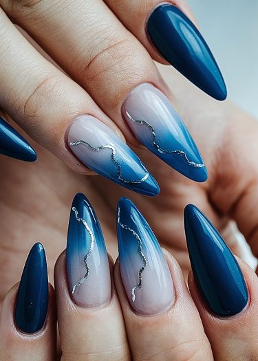 Elegant blue gradient stiletto nails with intricate silver accents and a glossy finish.