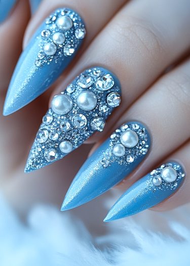 Stunning light blue stiletto nails adorned with pearls and rhinestones for a luxurious winter look.