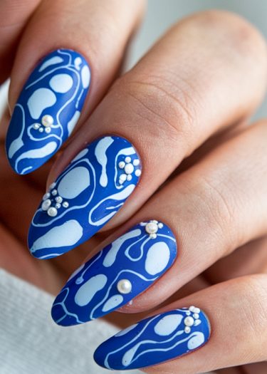 Elegant blue and white abstract nail art with pearls, showcasing intricate patterns and modern design.