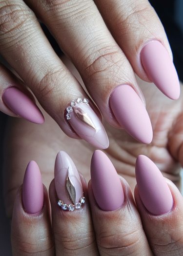 Elegant almond-shaped matte pink nails with rhinestones and rose gold accents.