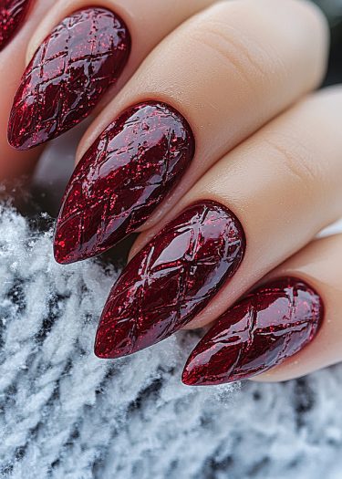 Elegant almond-shaped burgundy nails with quilted texture and glittery finish against a soft backdrop.