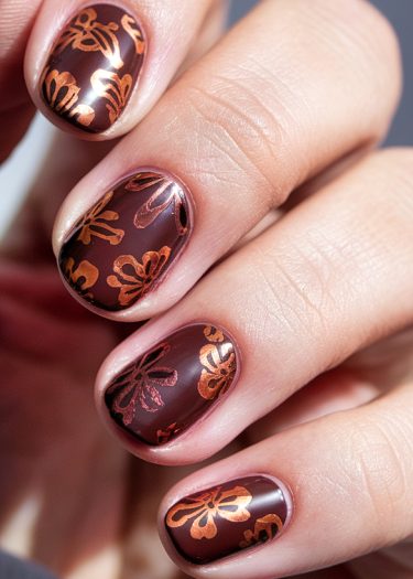 Elegant burgundy floral nail art with metallic copper designs and glossy finish.