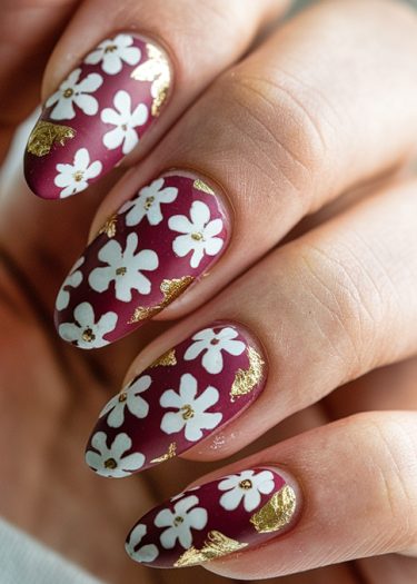 Elegant burgundy nail art with white floral designs and gold accents for a stylish manicure.