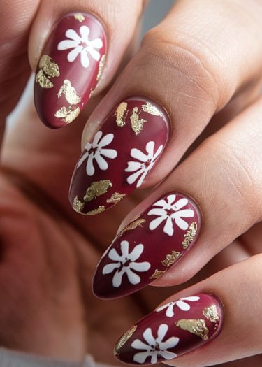 Elegant burgundy floral nail art with gold accents on almond-shaped nails.