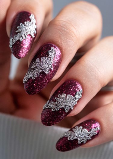 Elegant burgundy glitter nails with intricate silver floral designs for a glamorous look.