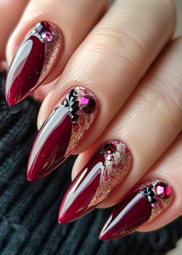 Elegant burgundy stiletto nails with gold glitter and rhinestones for a luxurious look.