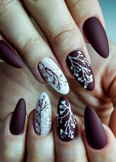 Elegant burgundy matte nails with artistic botanical designs and sparkling rhinestones.