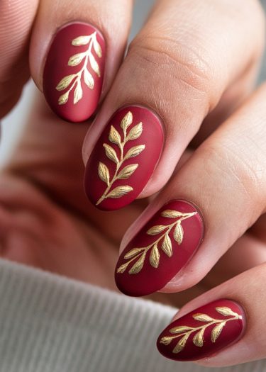 Elegant burgundy matte nails with gold leaf design for a sophisticated manicure look.