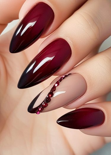 Elegant burgundy almond-shaped nails with gemstone accents for a sophisticated manicure design.